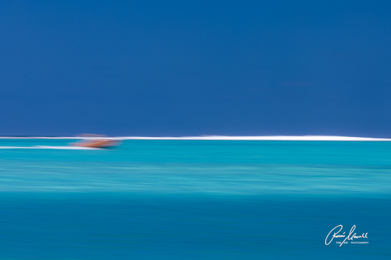 The blue waters of Bora-Bora on a sunny day when clouds came in changed the hue of the water while a small boat was cruising by.