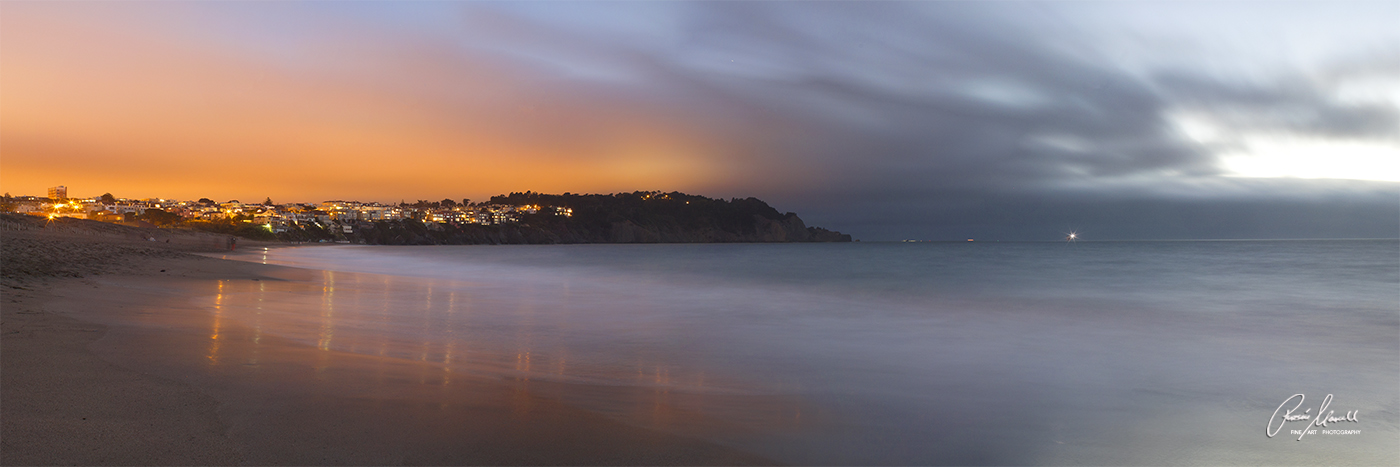 A panoramic image of a sunset with orange and blue hues over the ocean at Baker Beach in the Presidio of San Francisco, California