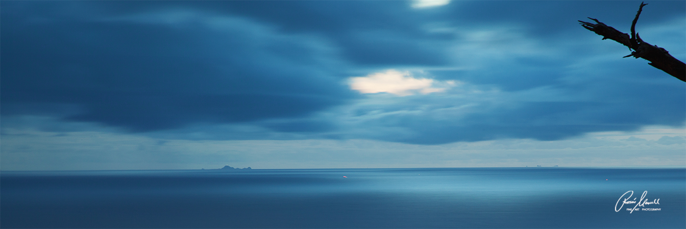 A moody blue view of the Farallon Islands on a clear and stormy day at sunset from San Francisco, CA. A panoramic fine art print...